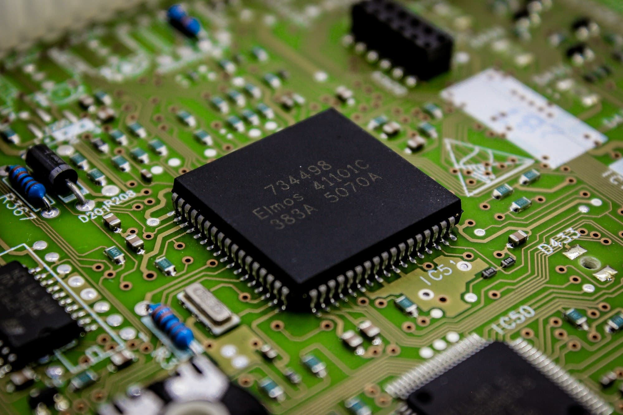 A close-up of a green circuit board with a black microchip at its center.