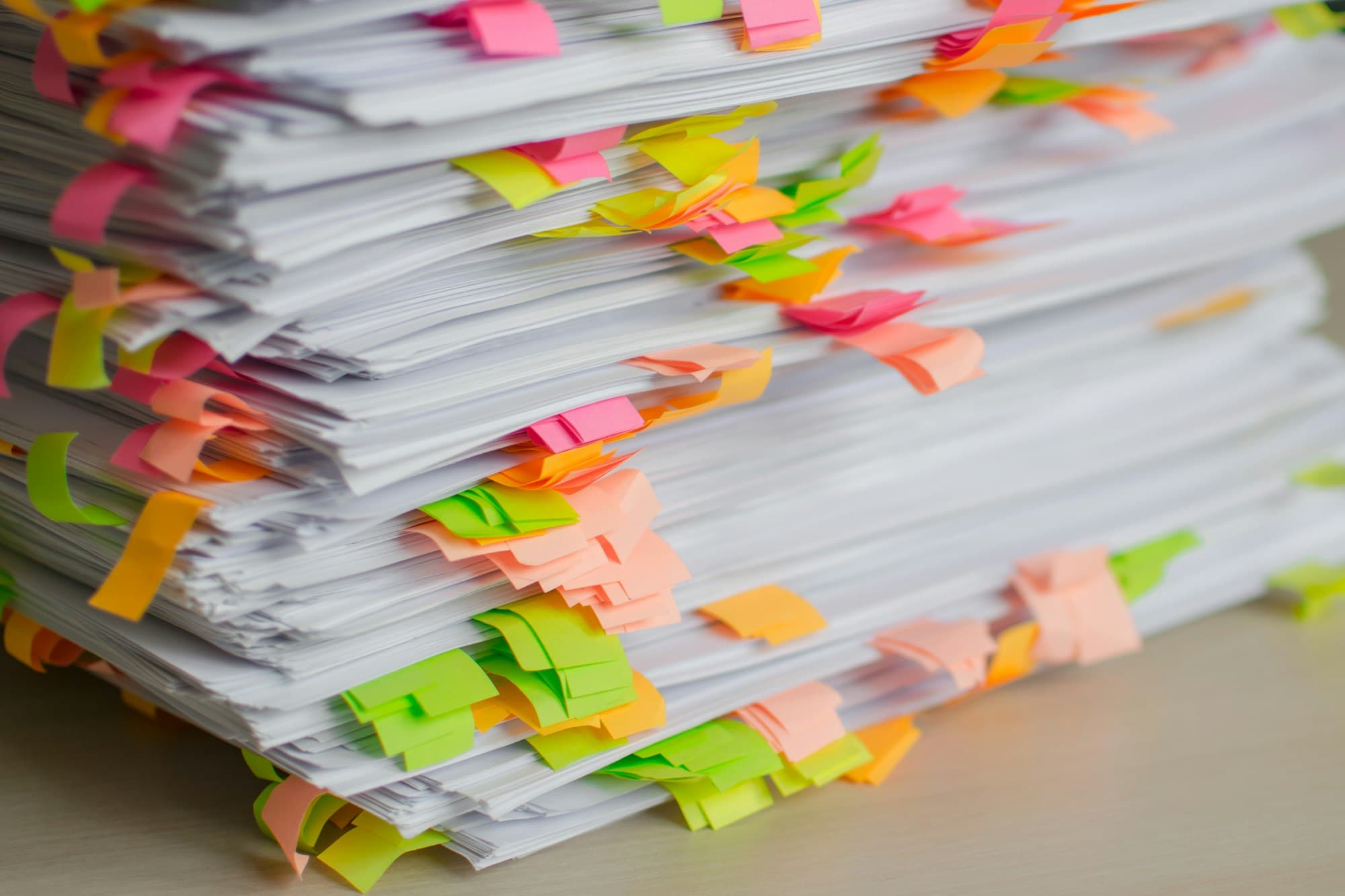 A tall stack of printed documents marked with dozens of pink, orange, yellow and green sticky tabs.
