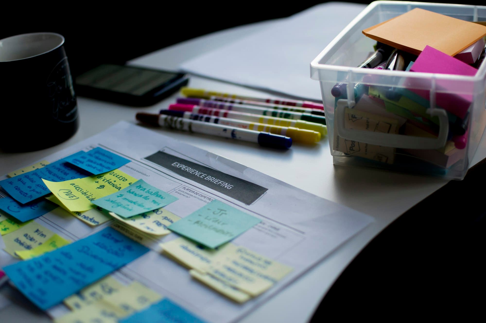 Blue, yellow and green sticky notes arranged on a printed planning sheet beside colored markers.